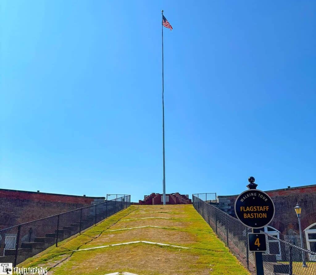 A tall flagpole with an American flag at Fort Monroe, surrounded by grassy slopes and historical brick architecture.