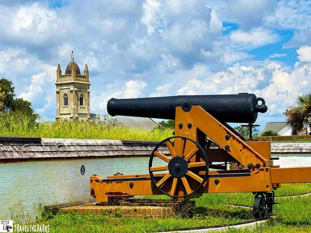 A historic cannon on a wooden carriage with a stone tower and cloudy sky in the background.