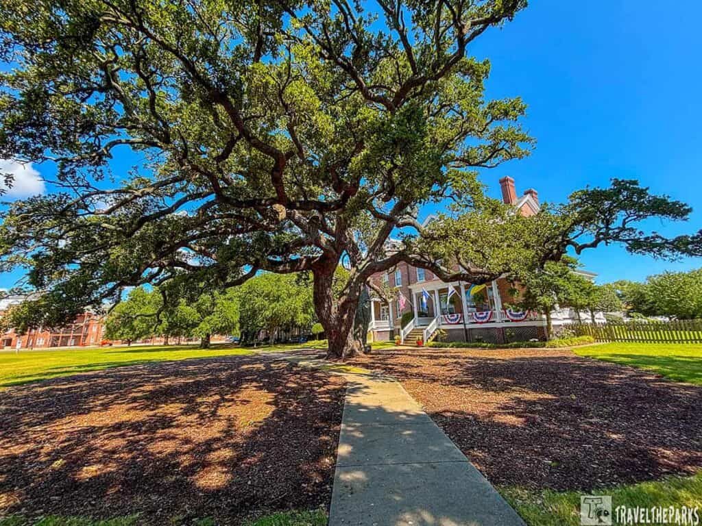 Historic white three-story building with porches and columns, wide staircase, and surrounding greenery under a blue sky.