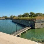 Fort Monroe National Monument with moat and bridge, surrounded by trees under a clear blue sky.