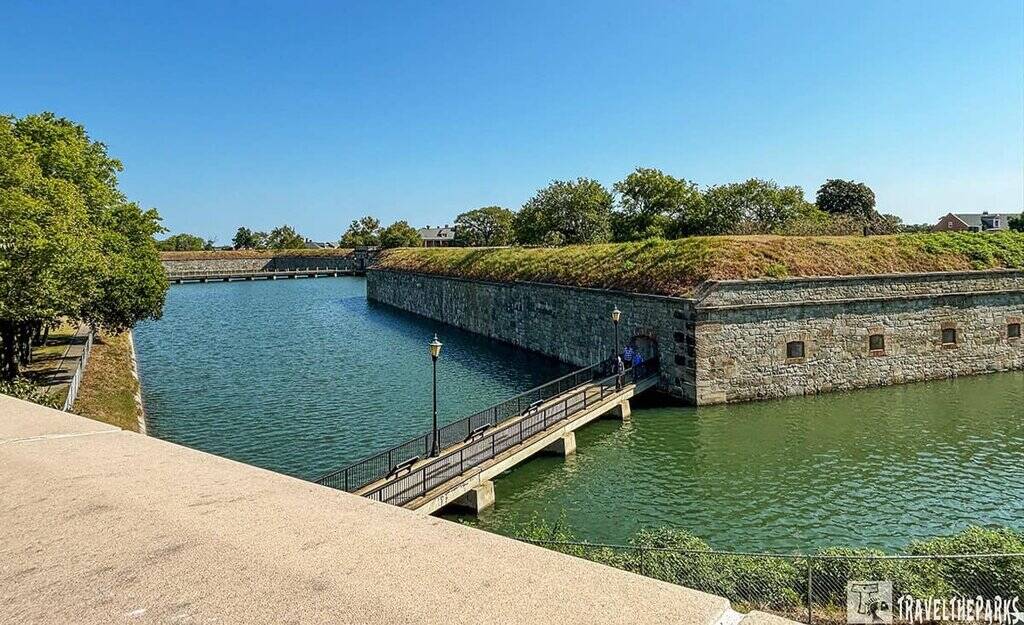Fort Monroe National Monument with moat and bridge, surrounded by trees under a clear blue sky.