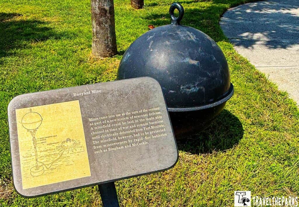 A spherical buoyant mine displayed on grass with an informational plaque.