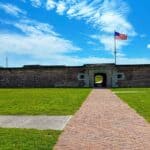 Fort Moultrie entrance with a brick pathway leading to an archway, and an American flag flying above.