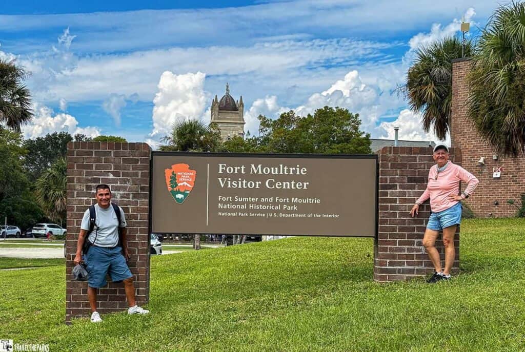 Two people posing beside a Fort Moultrie Visitor Center sign.