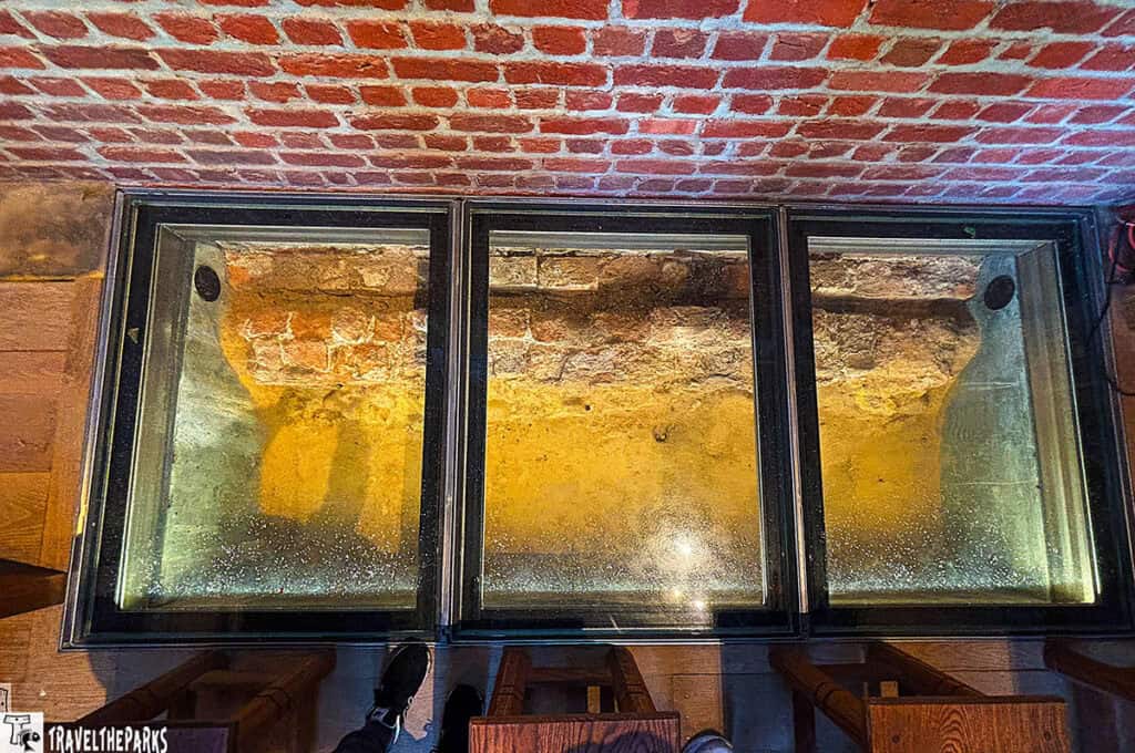Glass-enclosed view of the 1617 church foundation at Jamestown, displaying weathered bricks and soil.