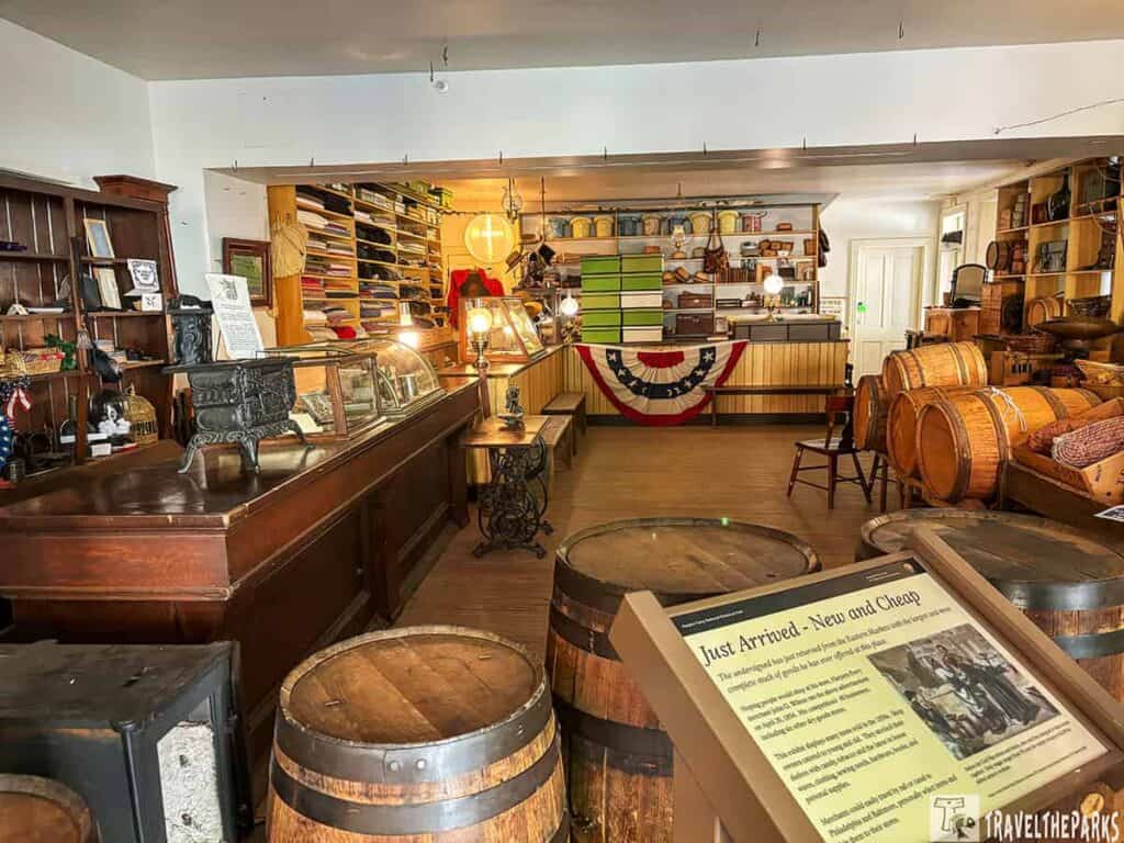 Interior of a historic general store with wooden barrels, display cases, and shelves filled with goods.

