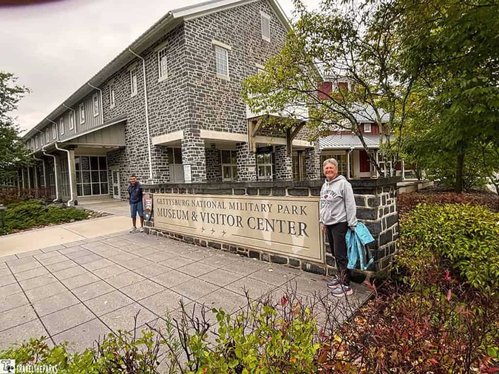 Entrance to Gettysburg National Military Park Museum & Visitor Center with a stone sign and two individuals standing nearby.