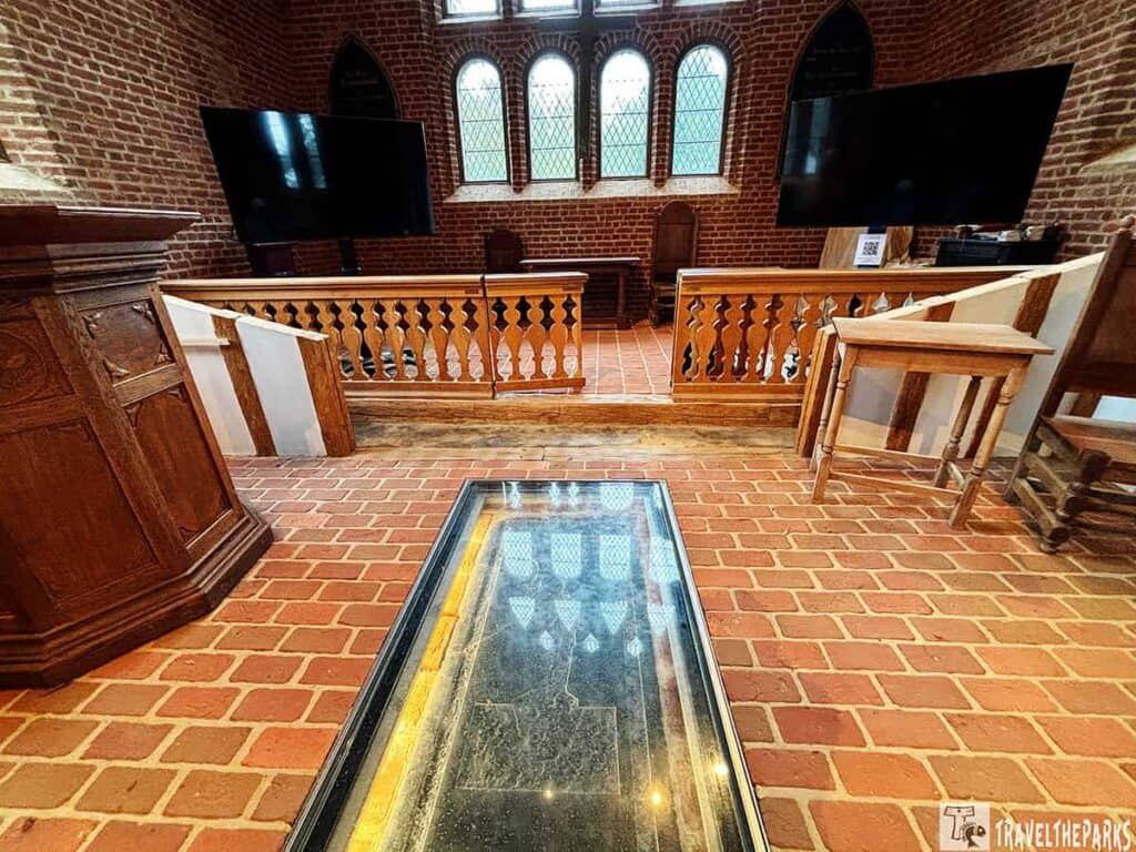 The Knight’s Tombstone in the Memorial Church. Interior of a historic church with a floor grave marker, wooden balustrade, stained glass windows, and brick walls.
