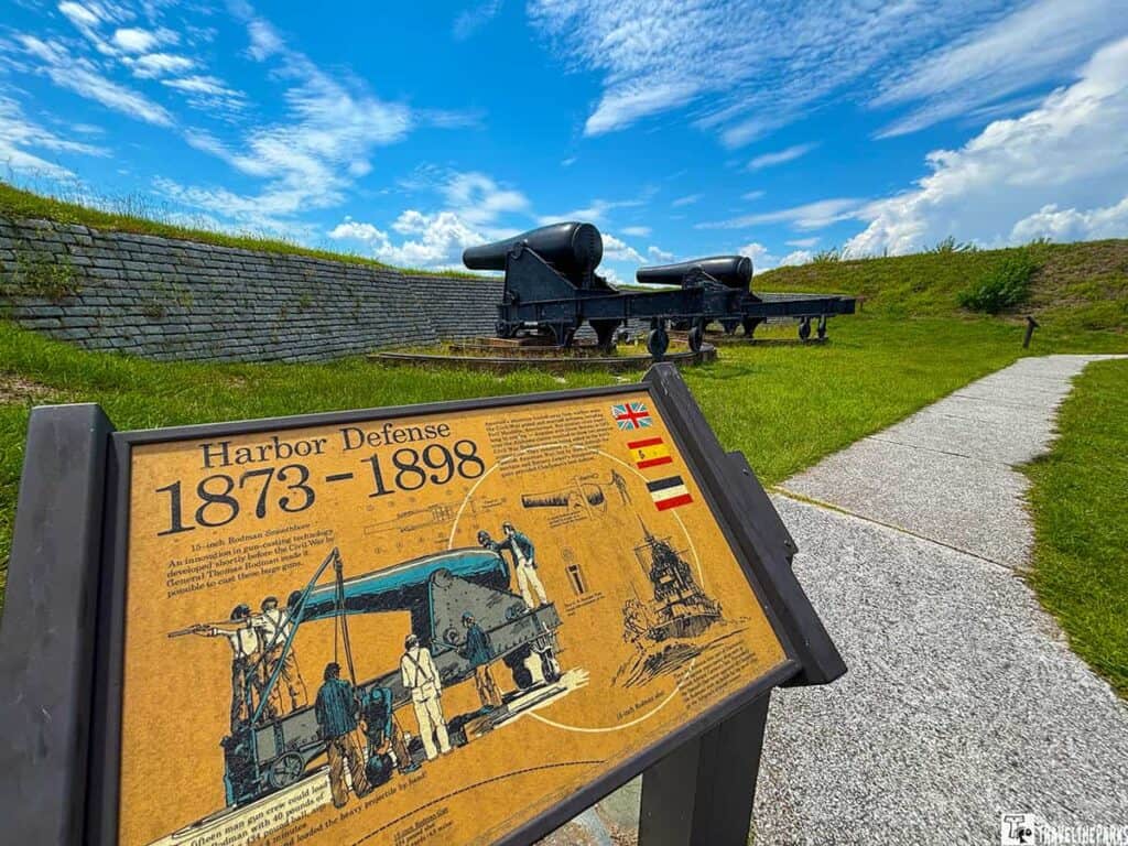 Historical site at Fort Moultrie with informational sign: Harbor Defense 1873 to 1898 and large cannons on a grassy area under a blue sky.
