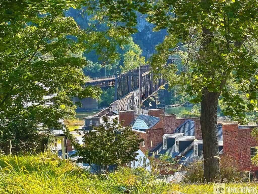 View of Harpers Ferry with a bridge over a river, framed by trees and surrounded by brick buildings.