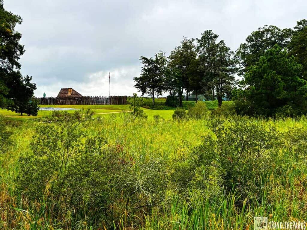 A view of Historic Jamestowne with lush greenery in the foreground and a reconstructed wooden fort in the background.