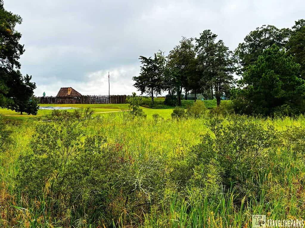 A view of Historic Jamestowne with lush greenery in the foreground and a reconstructed wooden fort in the background.