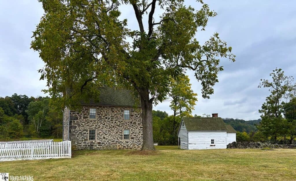 Stone building and white wooden house at John Slyder Farm, Gettysburg National Military Park, with a large tree and grassy landscape.