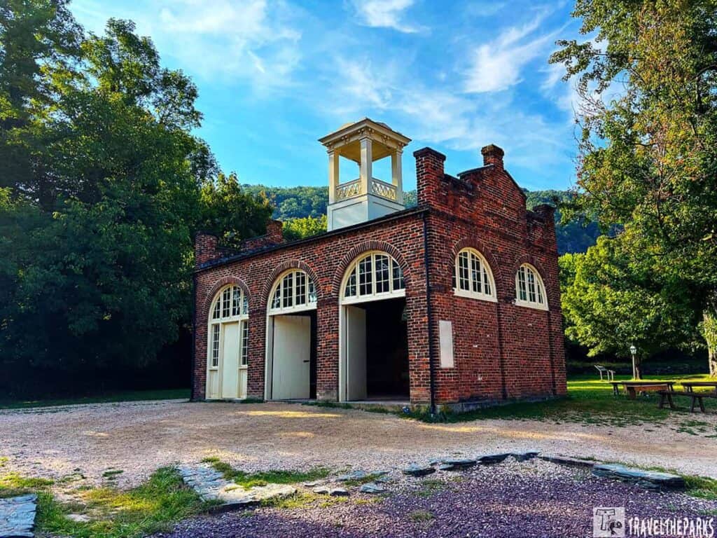 Historic John Brown brick firehouse with arched doors and a white cupola, surrounded by greenery.
