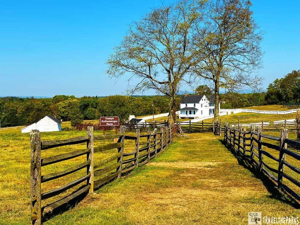 A rural landscape with wooden fences, a white farmhouse, and a sign reading "Joseph Poffenberger Farm."
