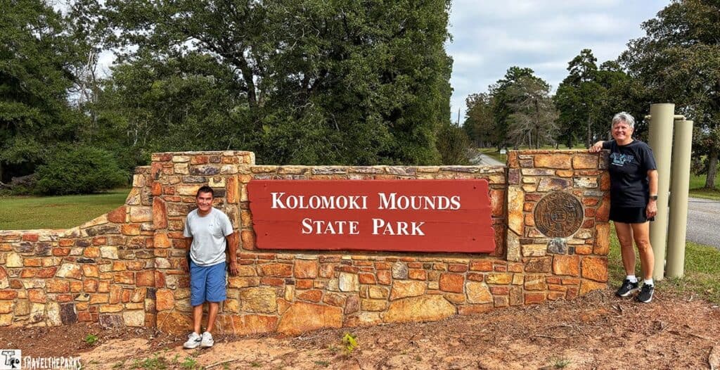 Stone sign for Kolomoki Mounds State Park with two people standing on either side.