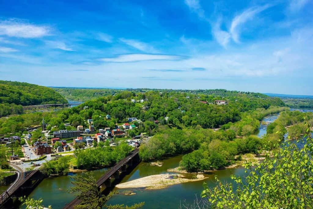 A small town surrounded by greenery with railway bridges crossing over rivers, under a blue sky.