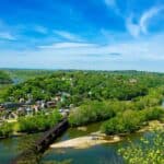 A small town surrounded by greenery with railway bridges crossing over rivers, under a blue sky.
