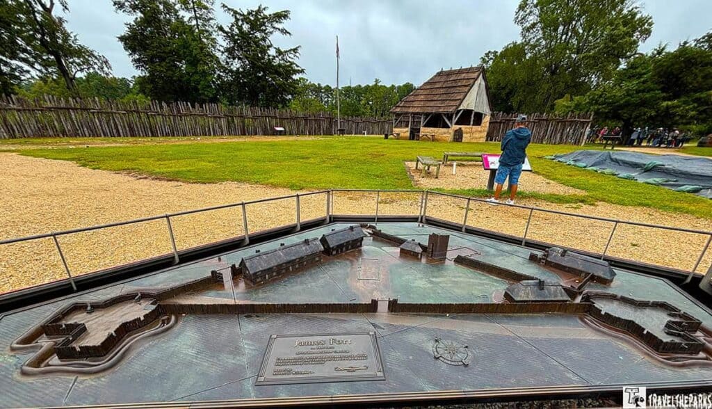 Bronze model of James Fort on Jamestown Island with reconstructed buildings and visitors in the background.