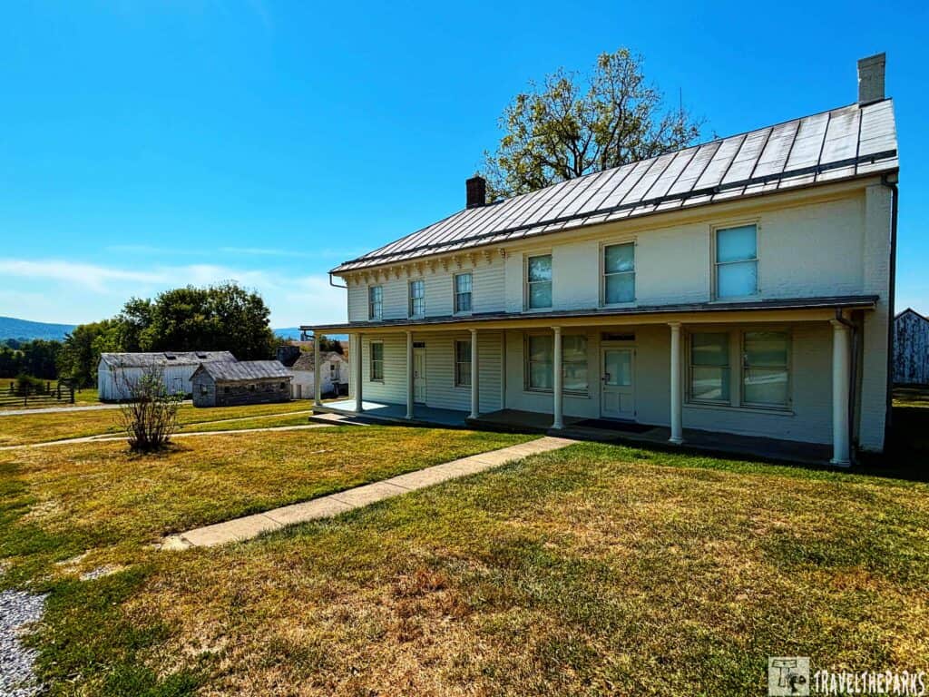 A white two-story Mumma farmhouse with a covered porch in a rural landscape.

