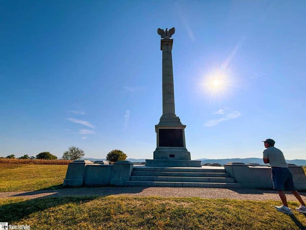 New York State Monument with a column and eagle topper against a clear sky at Antietam National Battlefield, with a person observing it.