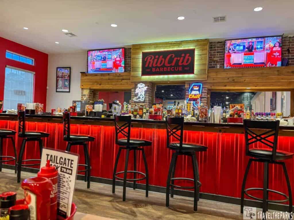 Interior view of RibCrib barbecue restaurant bar area with red highlights and black chairs.