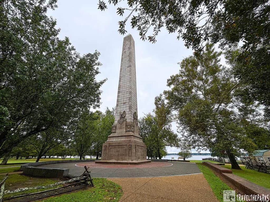 The Tercentenary-Monument stone obelisk surrounded by trees and located near water.