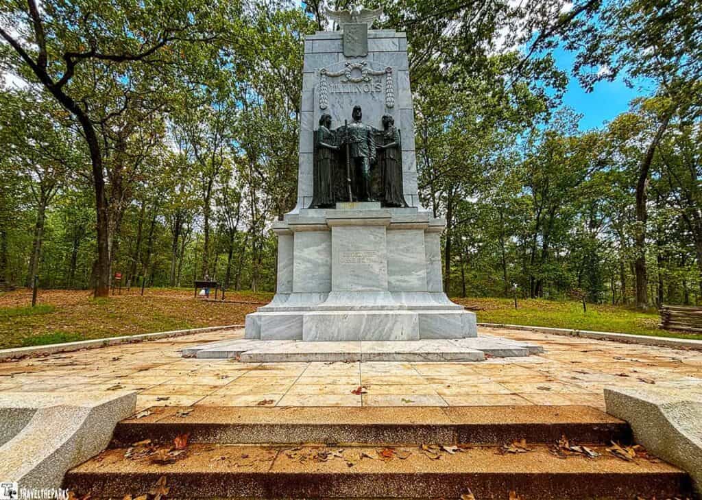 Stone monument in a wooded park, featuring soldier and draped figures.
