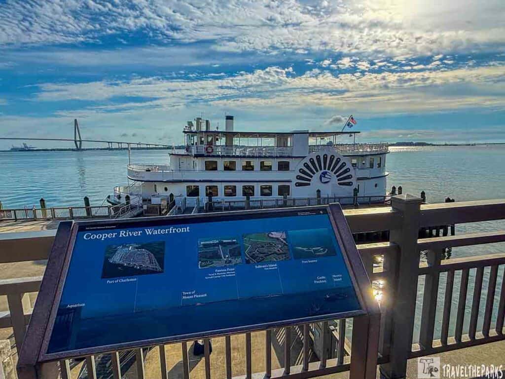 A riverboat docked at the Cooper River Waterfront with an informational display in the foreground.