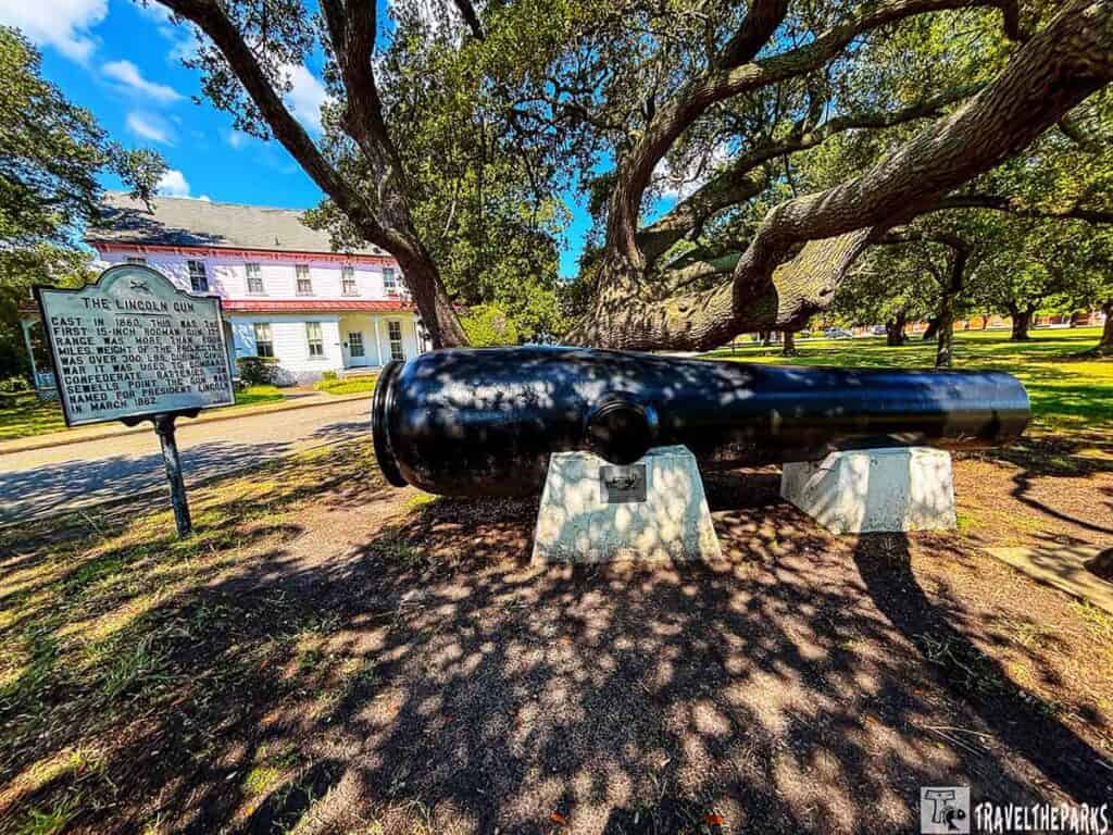 A large black cannon-the Lincoln Gun-under a tree with a historical sign, in front of a two-story building.

