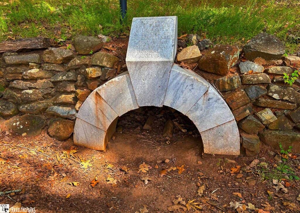 Stone tunnel entrance and wall with engraved capstone in a natural setting.