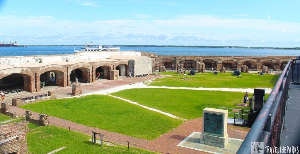 View of Union Garrison Monument and Parade grounds at Fort Sumter National Monument, with grass, brick pathways, historic fortifications, and a ferry boat.