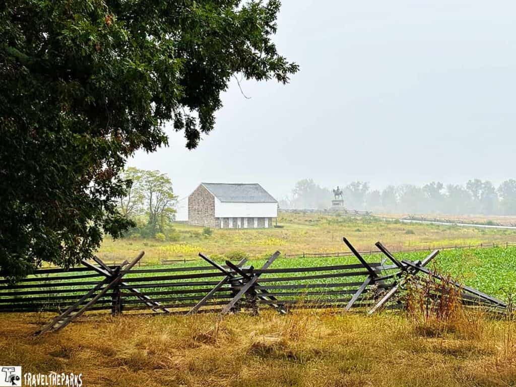 A barn and a horse statue at McPherson Farm in Gettysburg National Military Park with a wooden fence in the foreground.