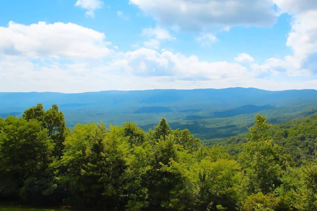 View of green hills and distant mountains under a blue sky with clouds.