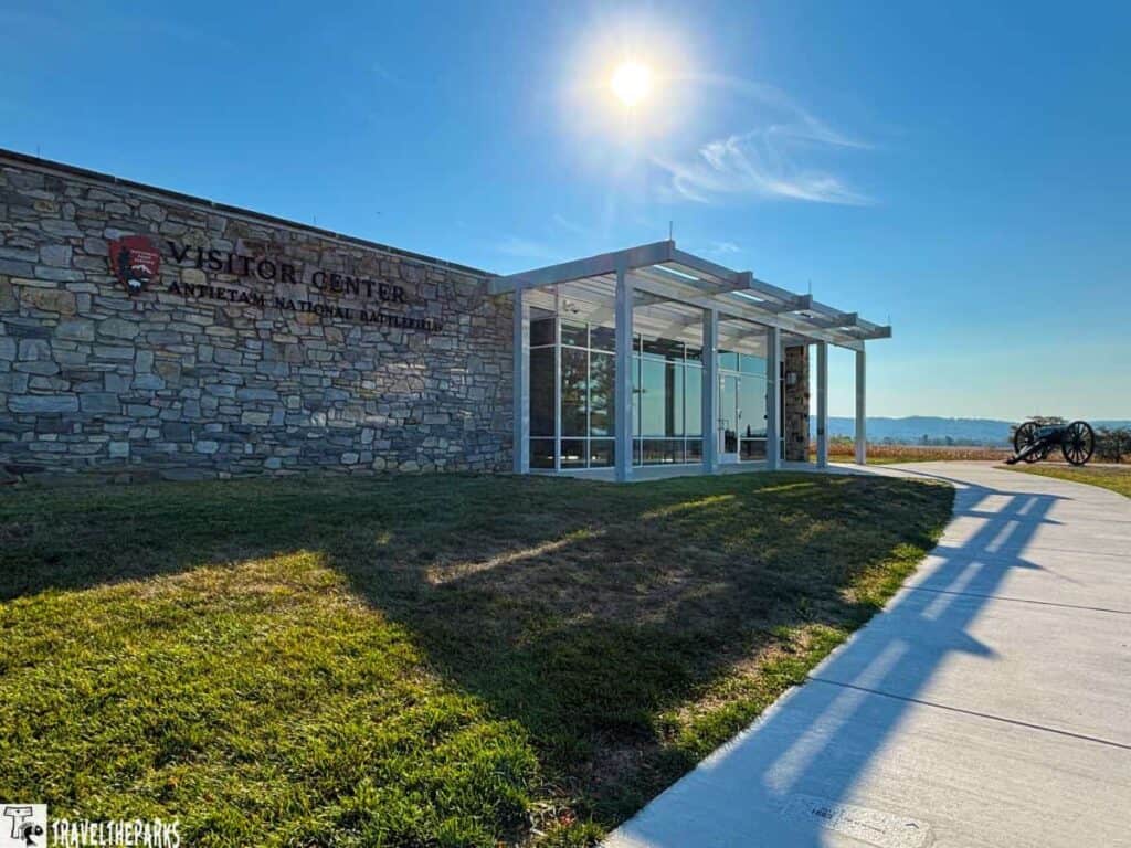 Antietam National Battlefield Visitor Center with a stone and glass structure, a cannon on the grassy field, and a bright sky.