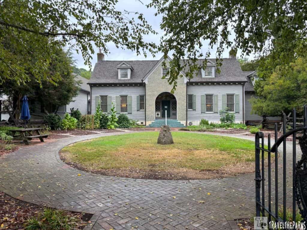 A historic gray wooden house with shutters, framed by a garden path and greenery.