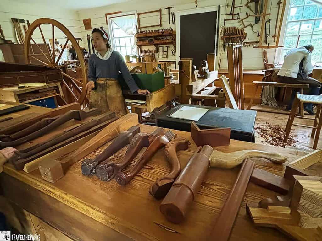 Interior of a woodworking shop with tools, wooden objects, and two people working.