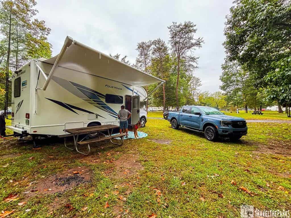 RV and truck in a grassy campground surrounded by trees.

