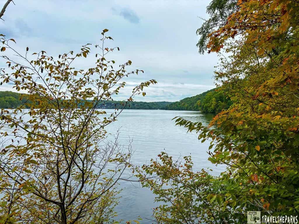 A calm lake surrounded by partially autumn foliage under a cloudy sky at Calytor Lake State Park.

