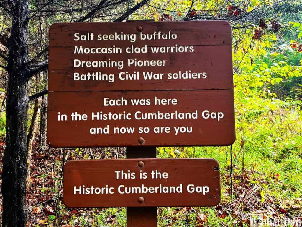 Wooden sign in a forest at Cumberland Gap National Historical Park displaying historical references and welcome text.