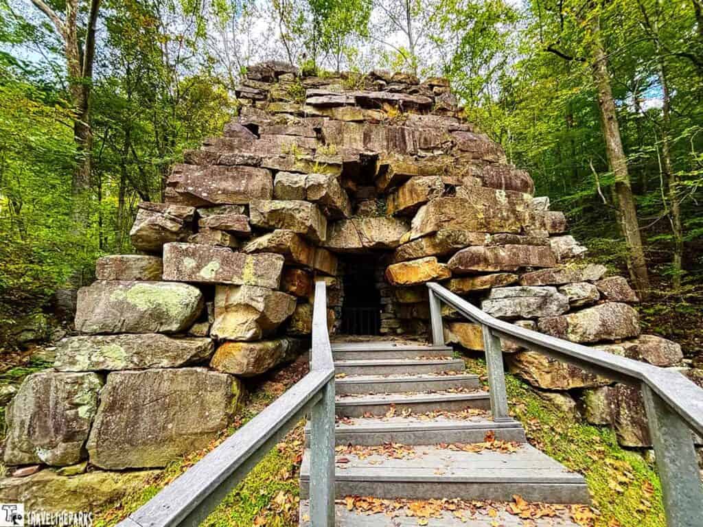 Stone iron furnace in a forest with stairs leading to its entrance.