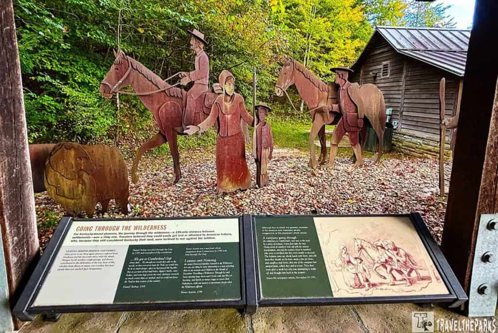 Daniel Boone Visitor Information Center metal silhouette display of pioneers and horses in a wooded area with a cabin in the background.