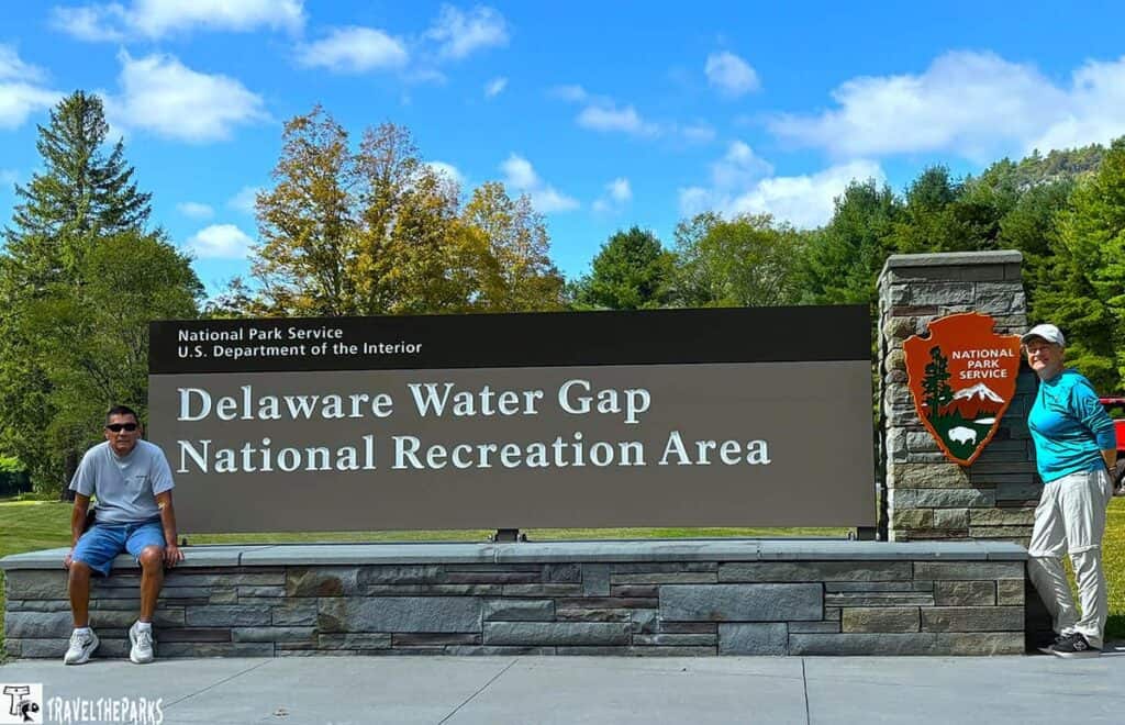 Sign for Delaware Water Gap National Recreation Area with two people posing and trees in the background.