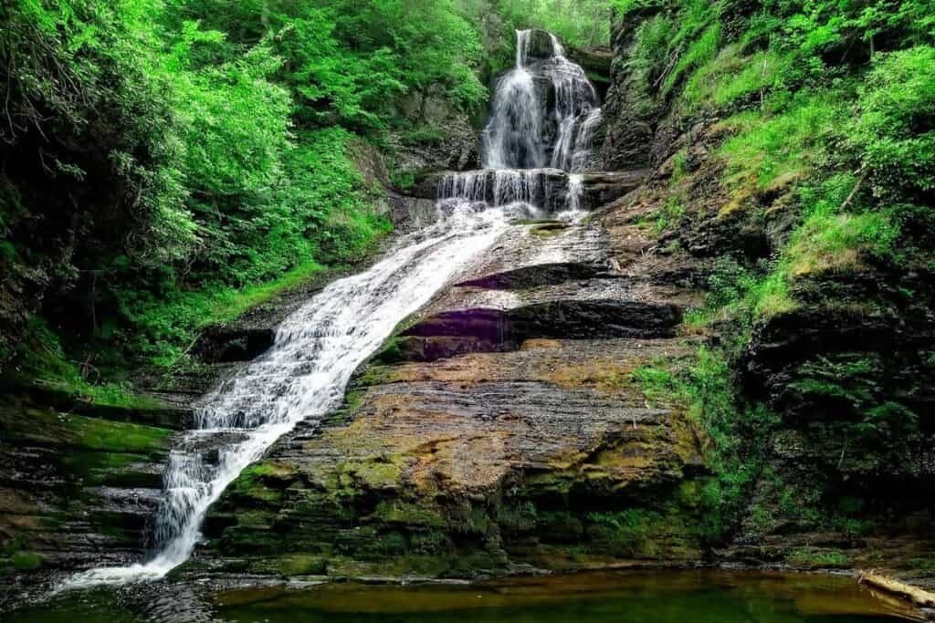 A cascading waterfall in the Delaware Water Gap, surrounded by lush greenery and rocky cliffs.