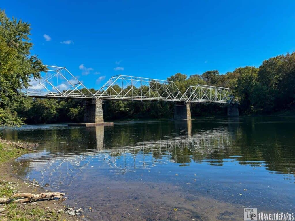 Dingmans Ferry Bridge over calm water with tree-lined banks and a clear blue sky.