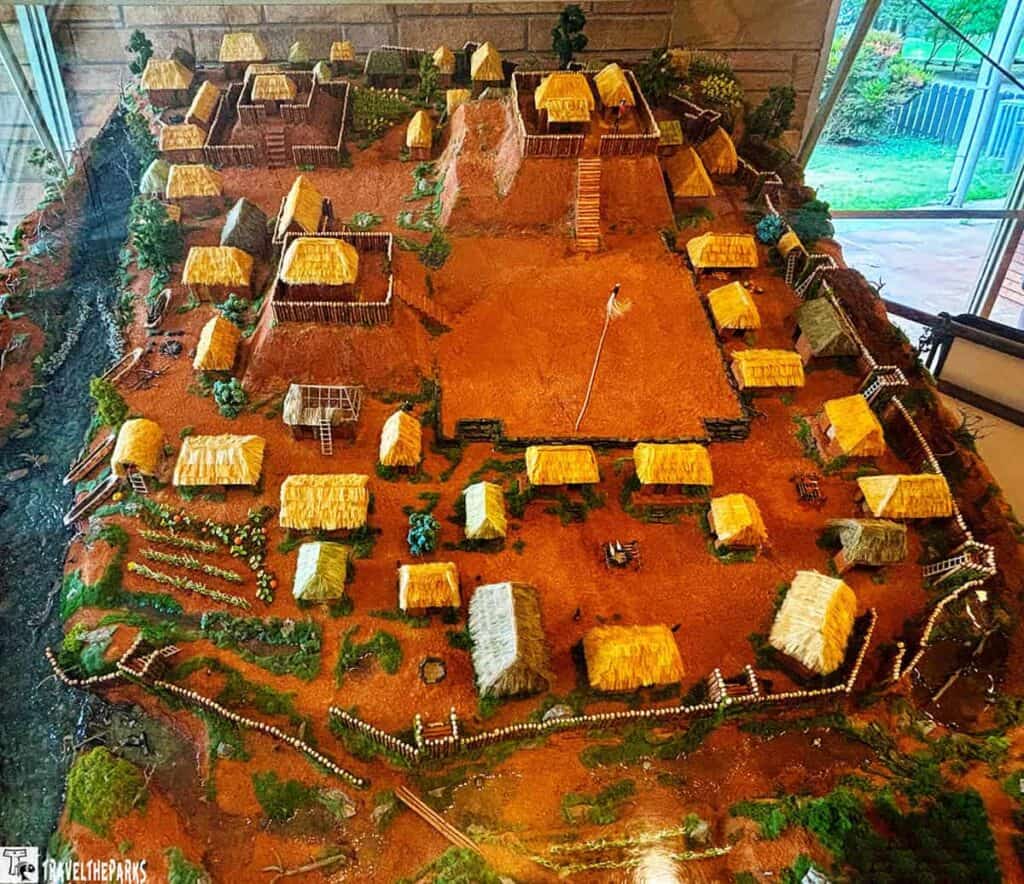 Model of Etowah Mounds with mounds, thatched structures, wooden palisade, and stream.


