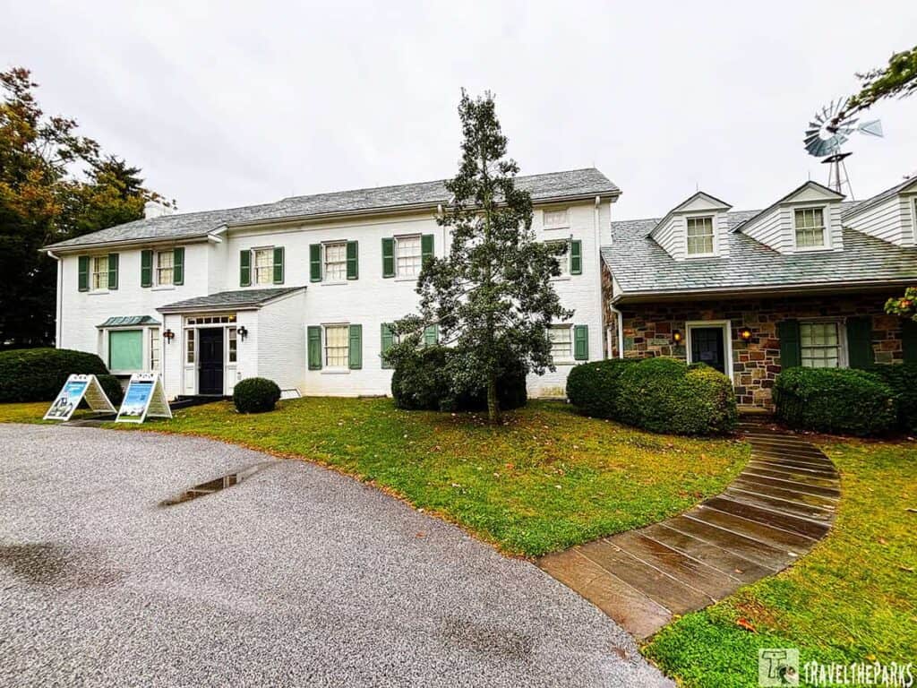 Two-story white brick house with green shutters, stone section, and a windmill at the Eisenhower National Historic Site.