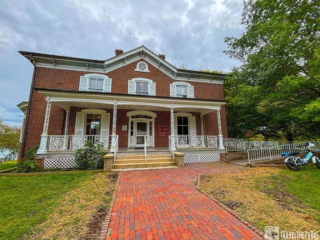 Front view of the brick Howe House with a porch and gabled roof at Clayton Lakes State Park.

