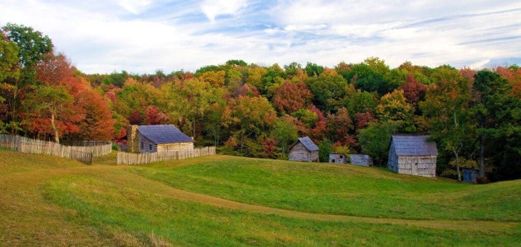 Hensley Settlement in autumn with old wooden cabins, green grass, and colorful fall trees.