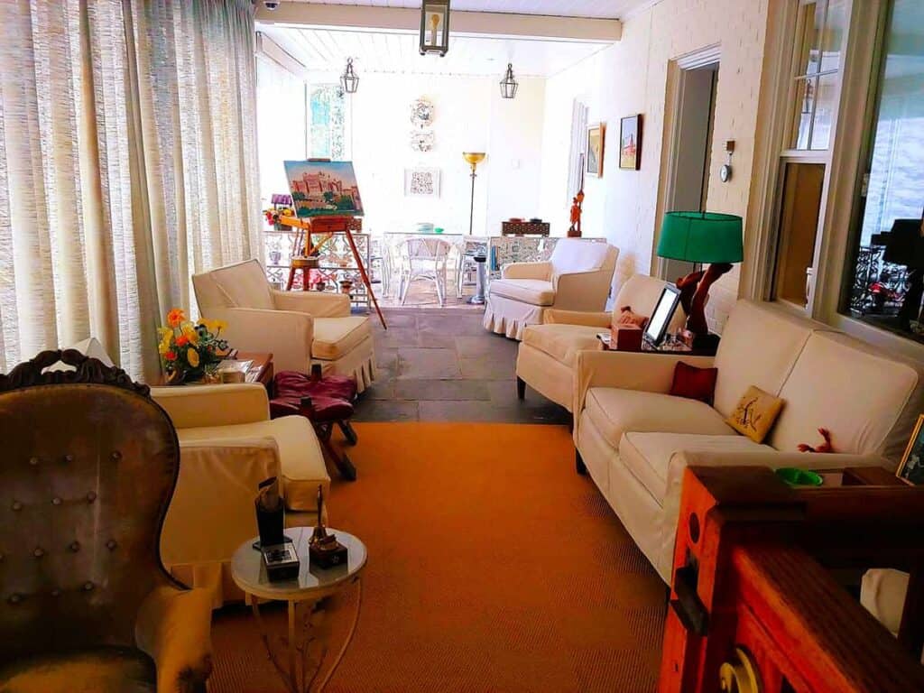 Sun porch with white furniture, sheer curtains, and an easel with a painting at Eisenhower National Historic Site.